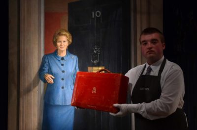 An employee holds a red Prime Ministerial dispatch box used by former British Prime Minister Margaret Thatcher, and expected to realise £3,000 - 5,000 GPB (4,100 - 6,900 euros) at auction, in front of a painting entitled 'Lady Thatcher on the steps of No.10 Downing Street' by Britsih artist Michael Noakes, during a photocall at Christie's auction house in central London on December 11, 2015, to promote their forthcoming auction "Mrs Thatcher: Property from the Collection of the Right Honourable The Baroness Margaret Thatcher of Kesteven," which is set to take place on December 15. The painting by Noakes will not form part of the sale, but is due to be auctioned separately. AFP PHOTO / BEN STANSALL RESTRICTED TO EDITORIAL USE, MANDATORY MENTION OF THE ARTIST UPON PUBLICATION, TO ILLUSTRATE THE EVENT AS SPECIFIED IN THE CAPTION / AFP / BEN STANSALL