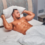 A handsome nude man lying in a bed.